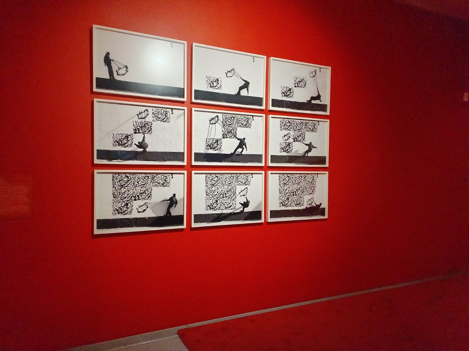 A sequence of framed black-and-white works on a red gallery wall